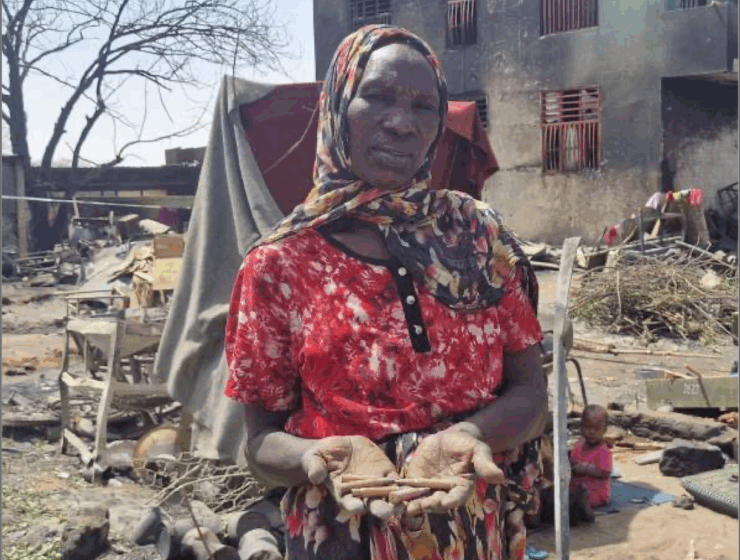 A Darfur woman standing in front of the ruins of a building, head covered in red dress.